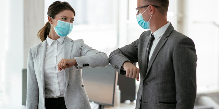 A businessman and businesswoman wear PPE masks and greet each other by touching elbows