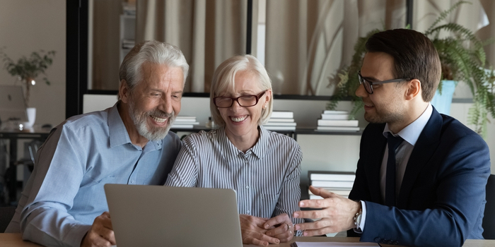 A young businessman talks to a senior couple in front of a laptop
